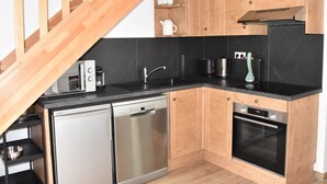 Une cuisine compacte avec des meubles en bois, un lave-vaisselle, une cuisinière et une machine à café.