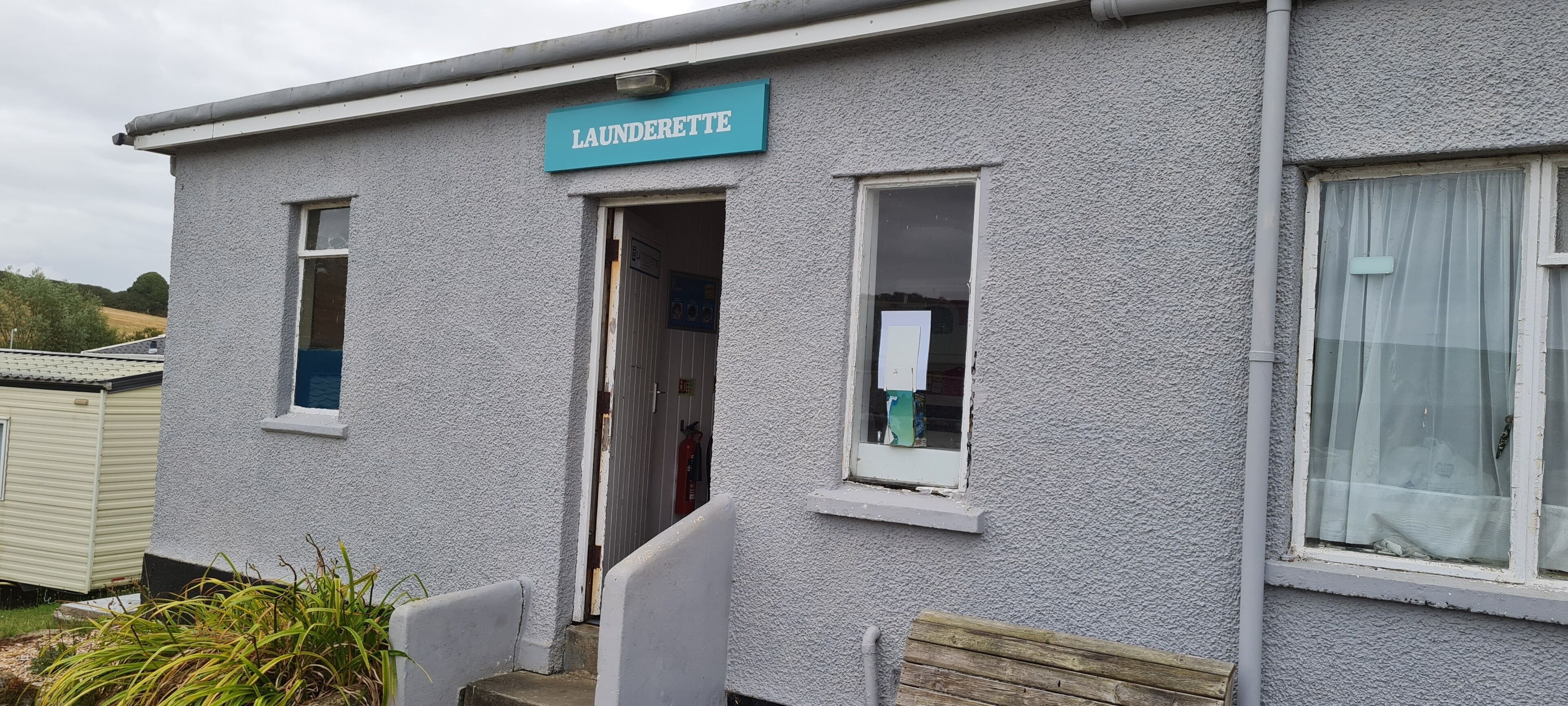 A building with a sign reading "LAUNDERETTE" and a door leading to an interior space.