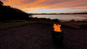Feuerstelle in Kiesnähe mit Sonnenuntergangblick über Wasser und Hügeln.