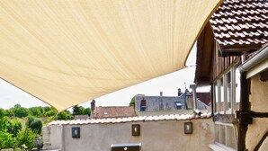 En udendørs terrasse med et bord, stole, grill og et skyggesejl.