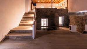 Un escalier menant à un mur de pierre, surmonté d’un plafond en bois, et offrant une vue sur l’intérieur.