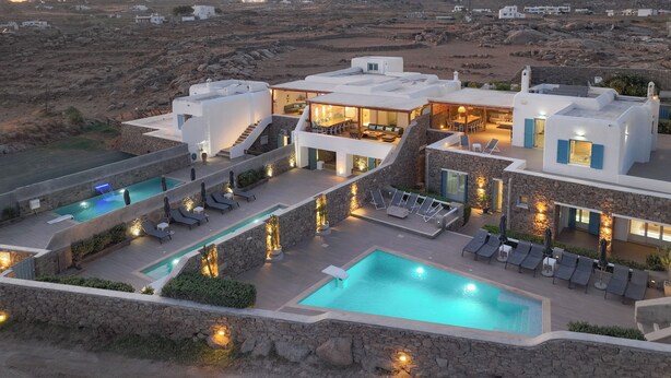 Une villa moderne dotée de plusieurs piscines, d’espaces de détente en plein air et d’une façade en pierre.