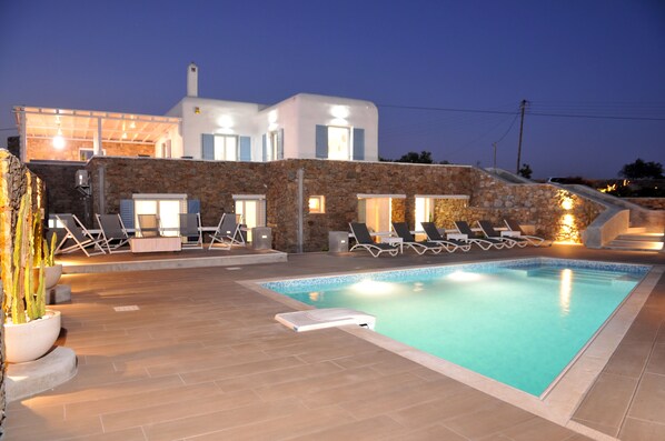 Un edificio moderno con piscina, pareti in pietra e poltrone relax.