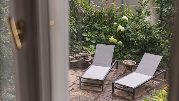 Two lounge chairs on a stone patio with a garden in the background.