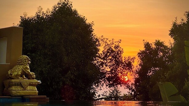 Ein Sonnenuntergang über einem Pool mit einer Löwenstatue und Bäumen im Hintergrund.