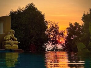 Un atardecer sobre una piscina con una estatua de león y árboles al fondo.