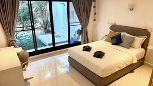 Ein modernes Hotelzimmer mit einem großen Bett, einem Schreibtisch und Blick auf einen Garten durch eine Schiebetür.