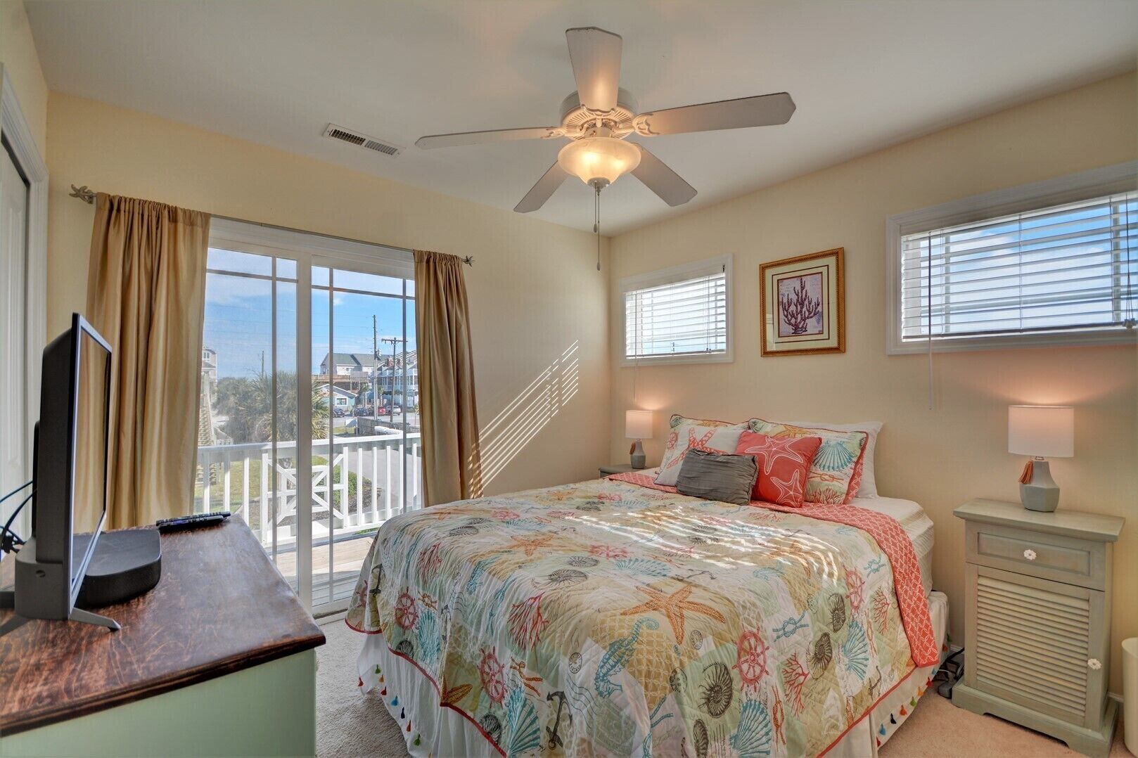 A bedroom with a bed, a desk, a ceiling fan, and a window with blinds.