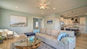 A modern living room with a glass coffee table, a beige sofa with patterned cushions, and a blue patterned rug. - Gorgeous Newly Built Home: Golf Course View! (Brigantine)