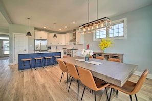 A modern kitchen with a central island, bar stools, and a dining table with chairs.