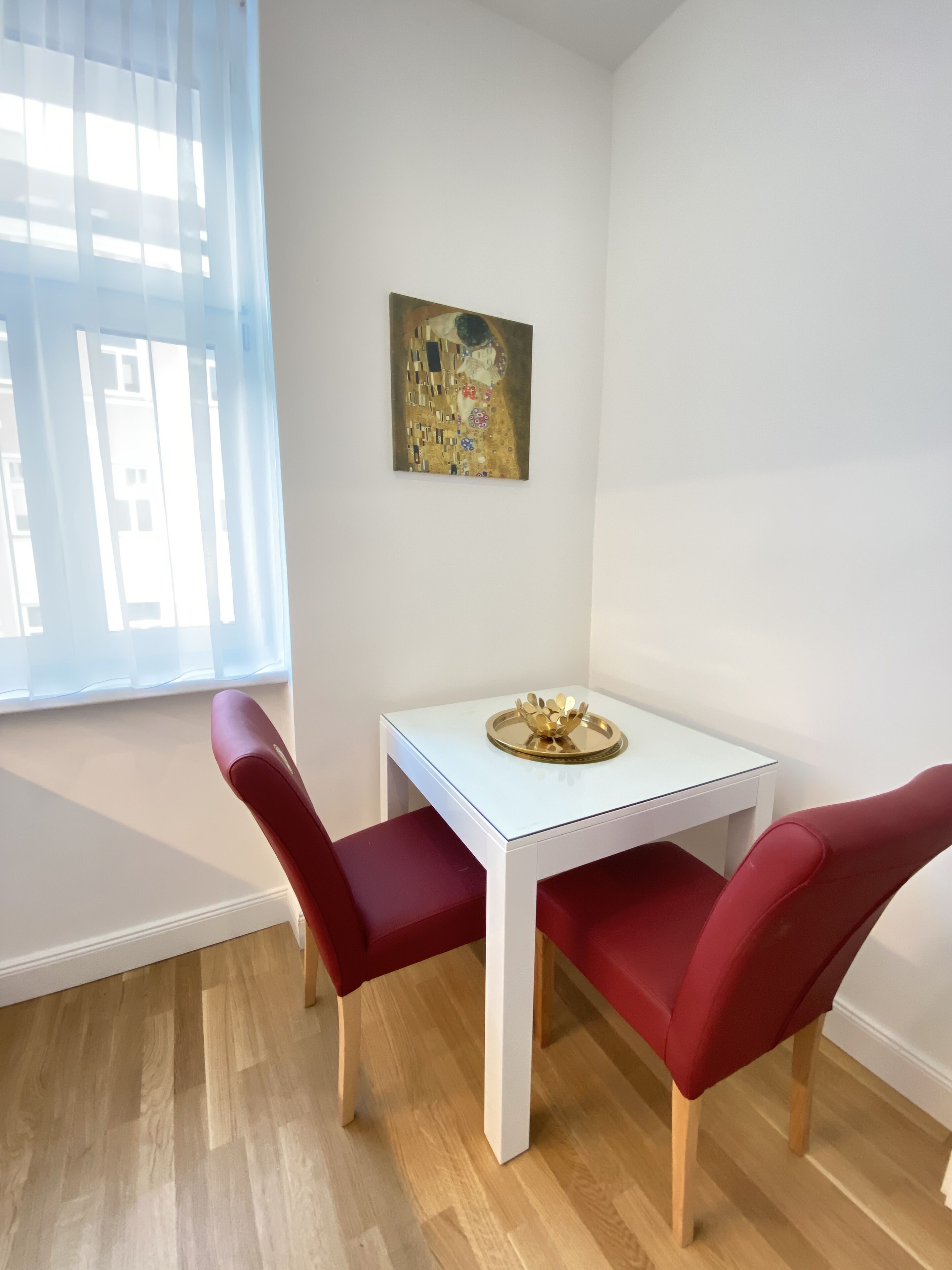 Un coin repas avec une table blanche, des chaises rouges et un tableau accroché au mur.