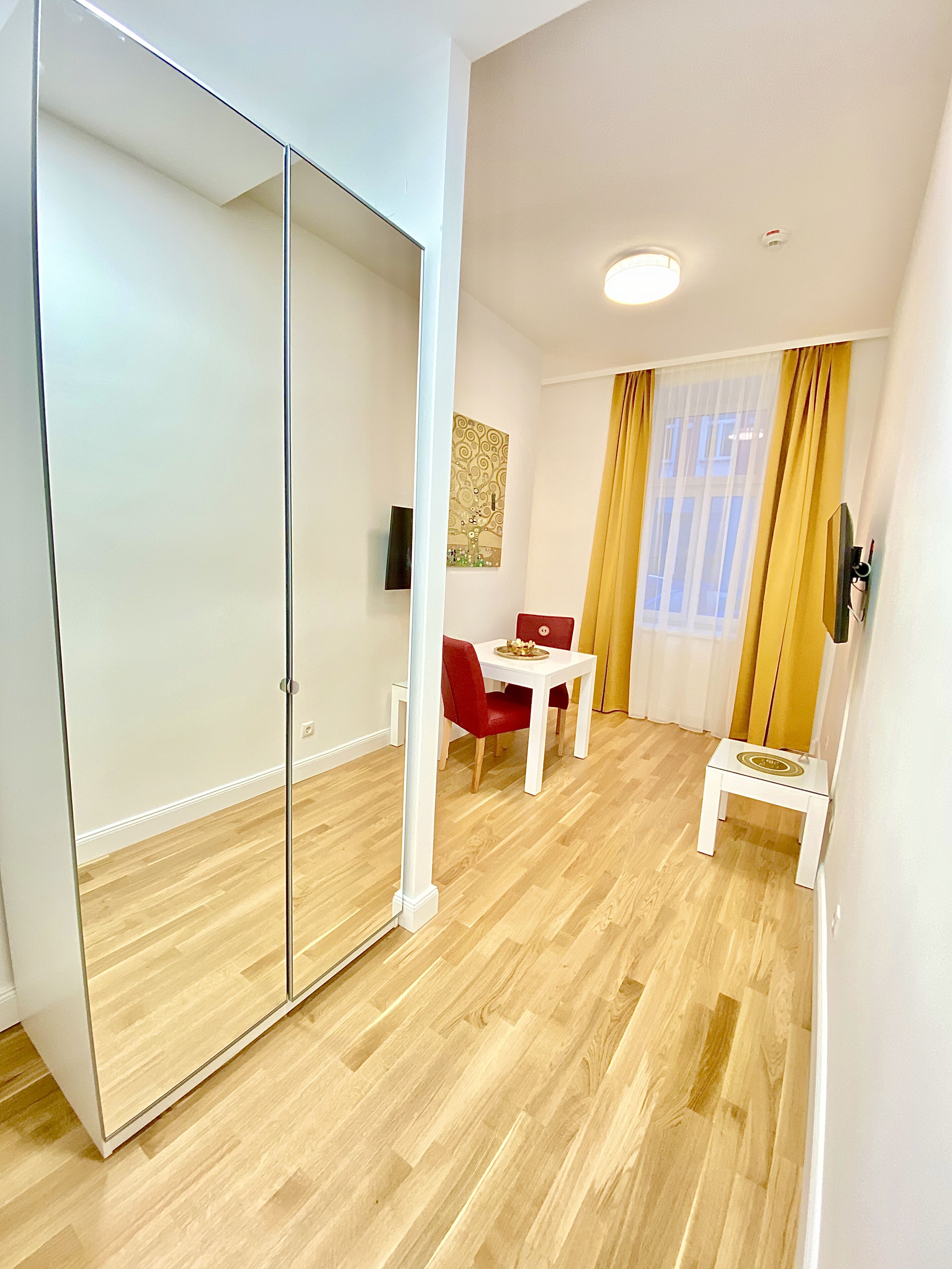 Una habitación moderna con piso de madera, un separador de vidrio, una mesa de comedor con sillas rojas y una pequeña mesa blanca con un adorno.