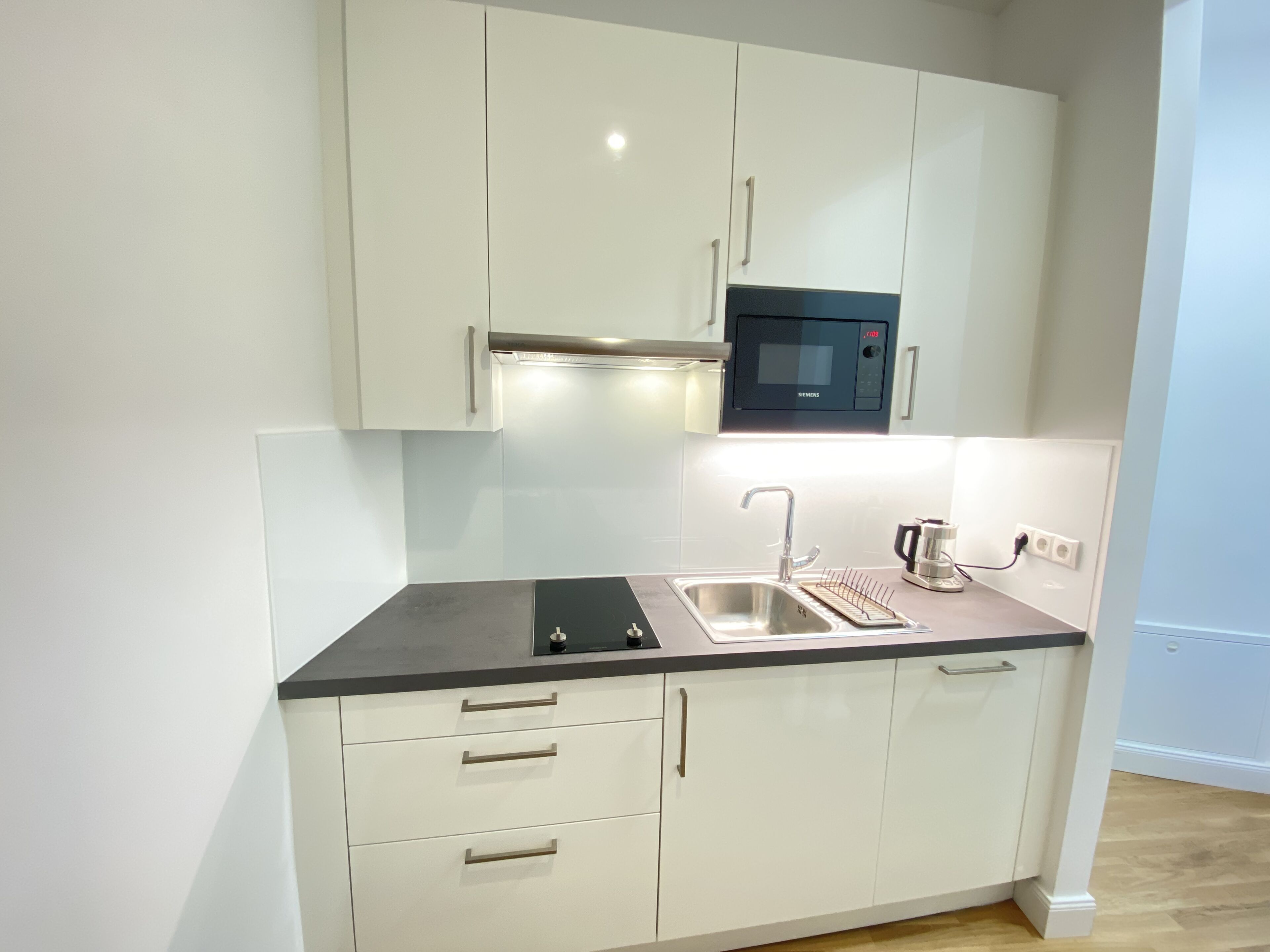 A modern kitchen with white cabinets, a black countertop, a built-in microwave, a sink, and a coffee maker.