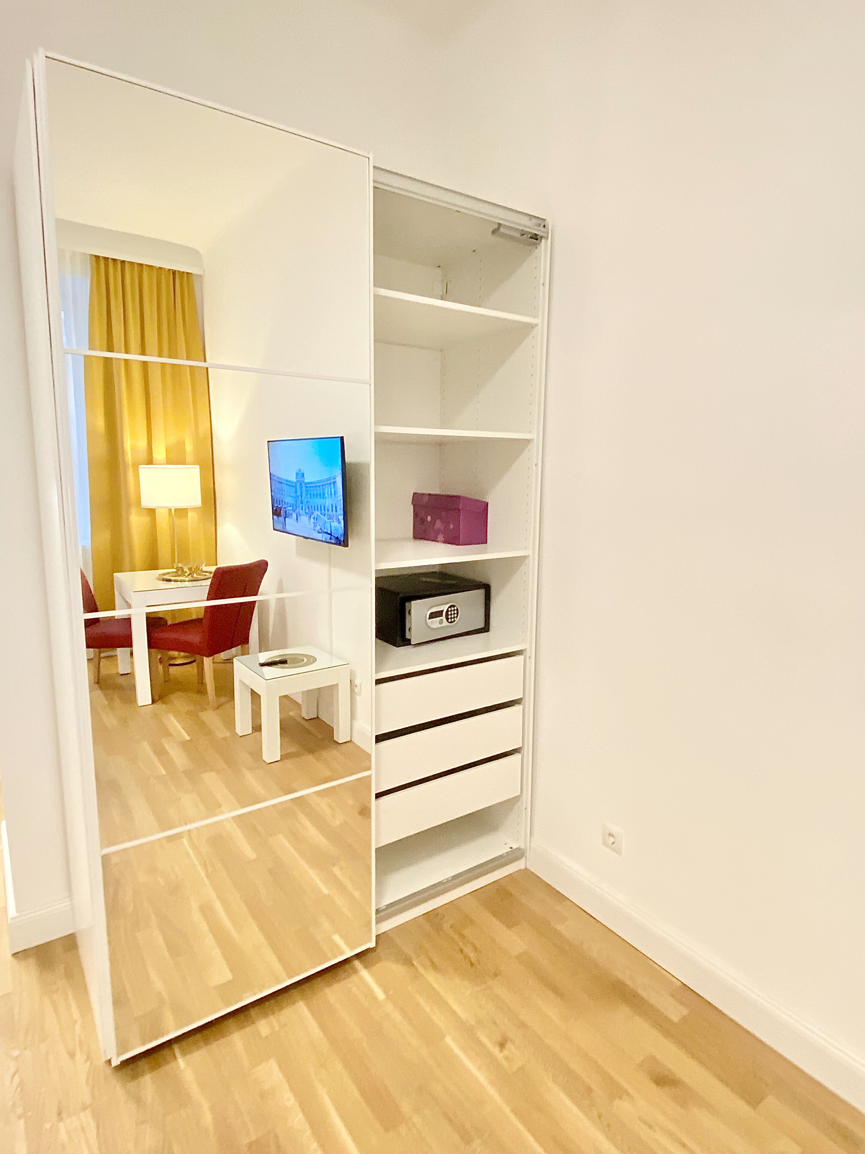 A room with a white wardrobe, a television, a small table, and a chair.