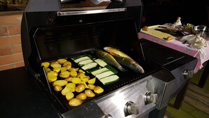 Un barbecue avec des pommes de terre, des courgettes et du poisson.