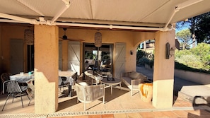 An outdoor patio area with tables and chairs, a ceiling fan, and a view of the garden.