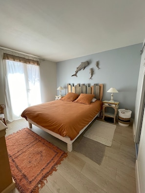 A bedroom with a bed, two nightstands, a rug, a wall-mounted shelf, and a window with curtains.