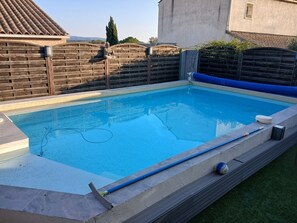 A swimming pool with a wooden fence, a statue, and a hose.