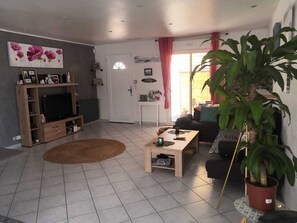 A living room with a TV, sofa, coffee table, and a large potted plant.