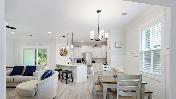 Une cuisine moderne avec des meubles blancs, un îlot central et un coin repas comprenant une table et des chaises en bois.