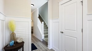 Un couloir avec un escalier, des portes blanches et une petite table ornée d’objets décoratifs.