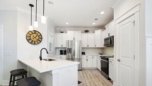 Une cuisine moderne avec des meubles blancs, des appareils en acier inoxydable et des luminaires suspendus.