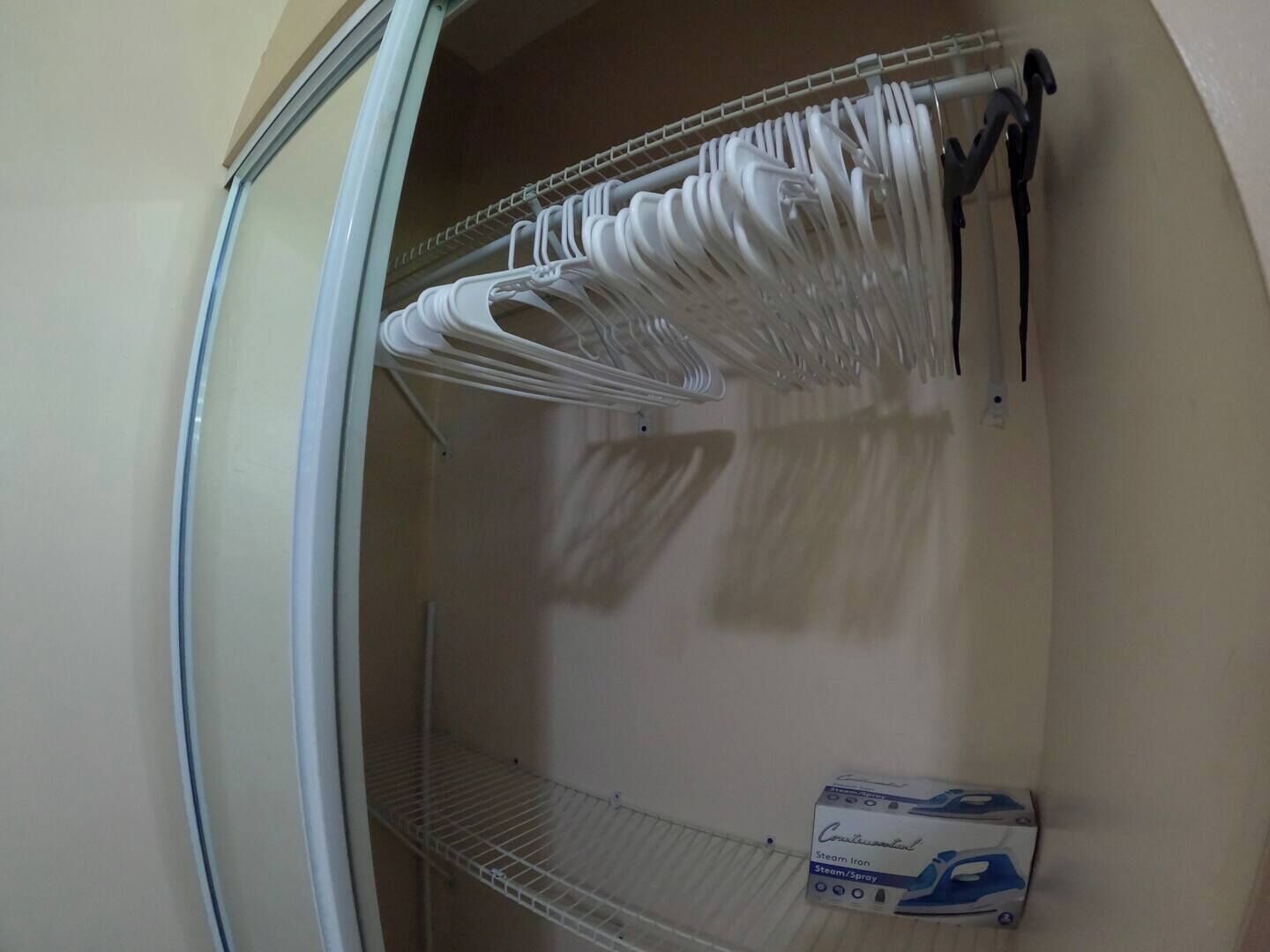 Un placard avec des cintres blancs et un fer à repasser à vapeur.