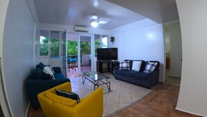 Un salon avec un canapé, un fauteuil jaune, un téléviseur et un balcon équipé d’une table et de chaises.