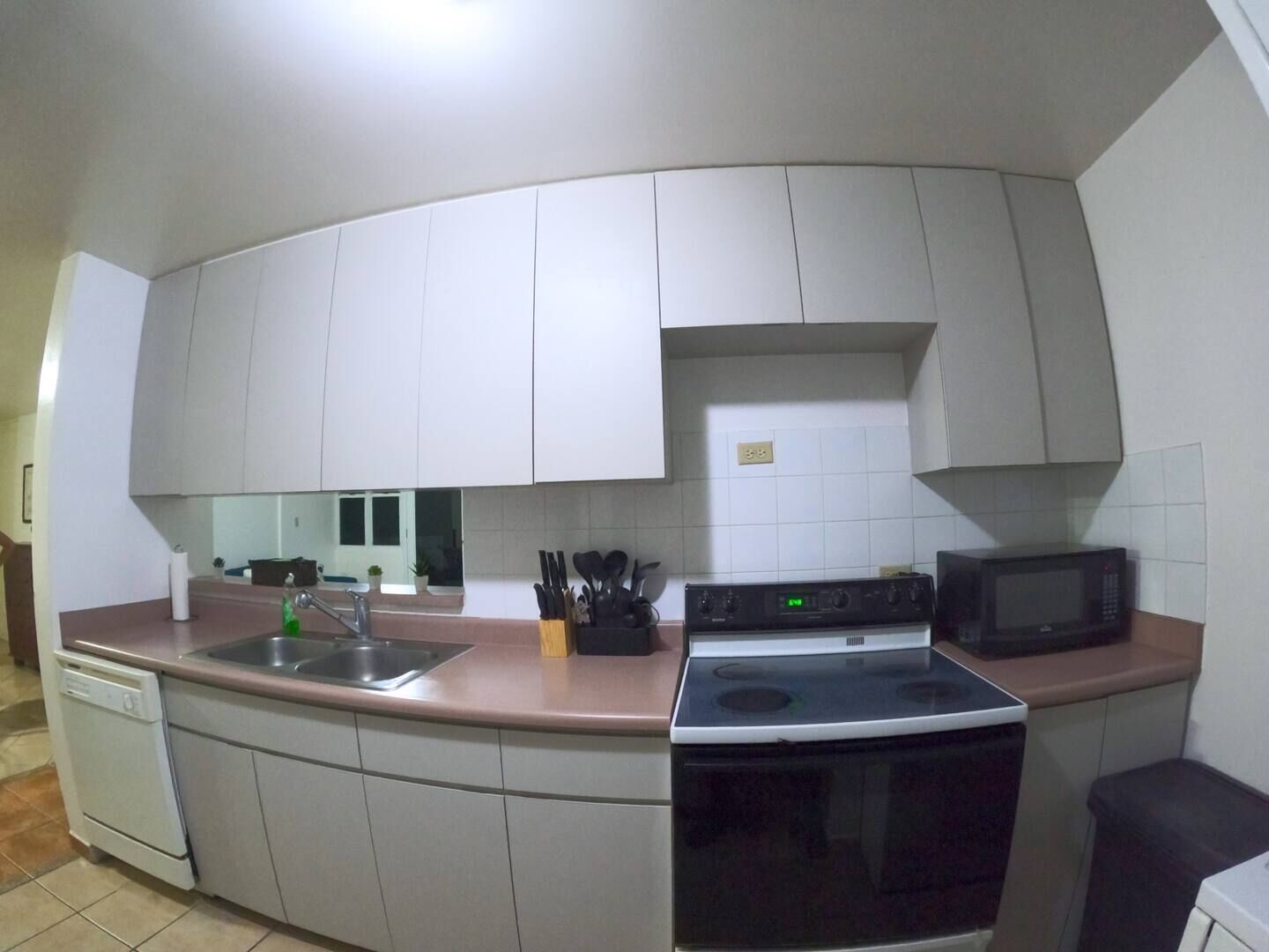 A kitchen with white cabinets, a stove, a microwave, and a sink.