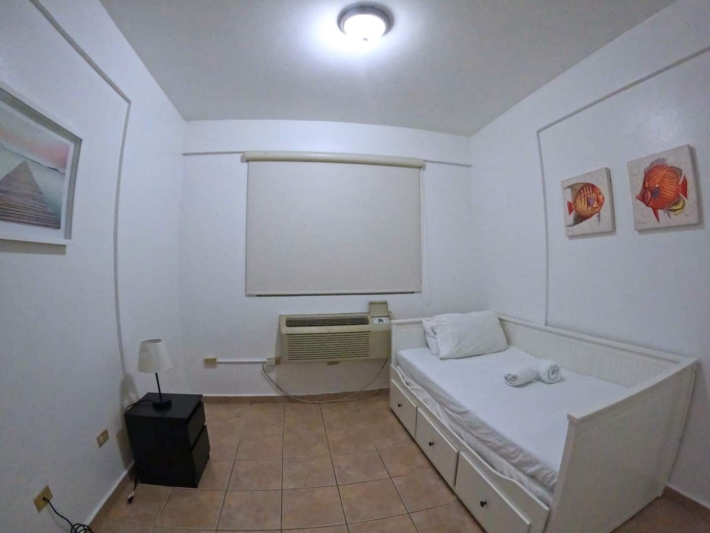 A small, clean room with a bed, a desk, and a window.