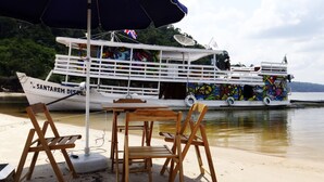 A boat named 'SANTAREM DISCO' docked at a beach with wooden chairs and an umbrella. - Gorgeous Converted Fishing Vessel in Alter do Chao (Santarém)