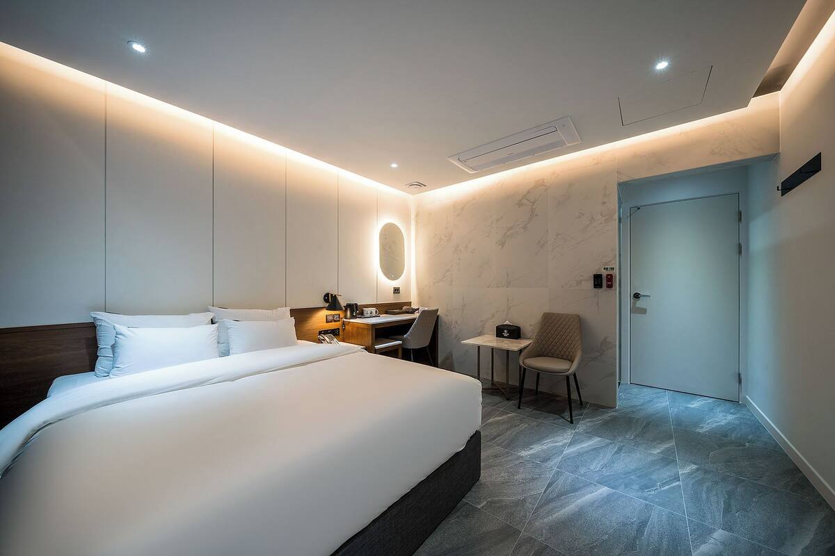 Ein modernes Hotelzimmer mit einem großen Bett, einem Schreibtisch, einem Stuhl und einem kleinen Tisch.