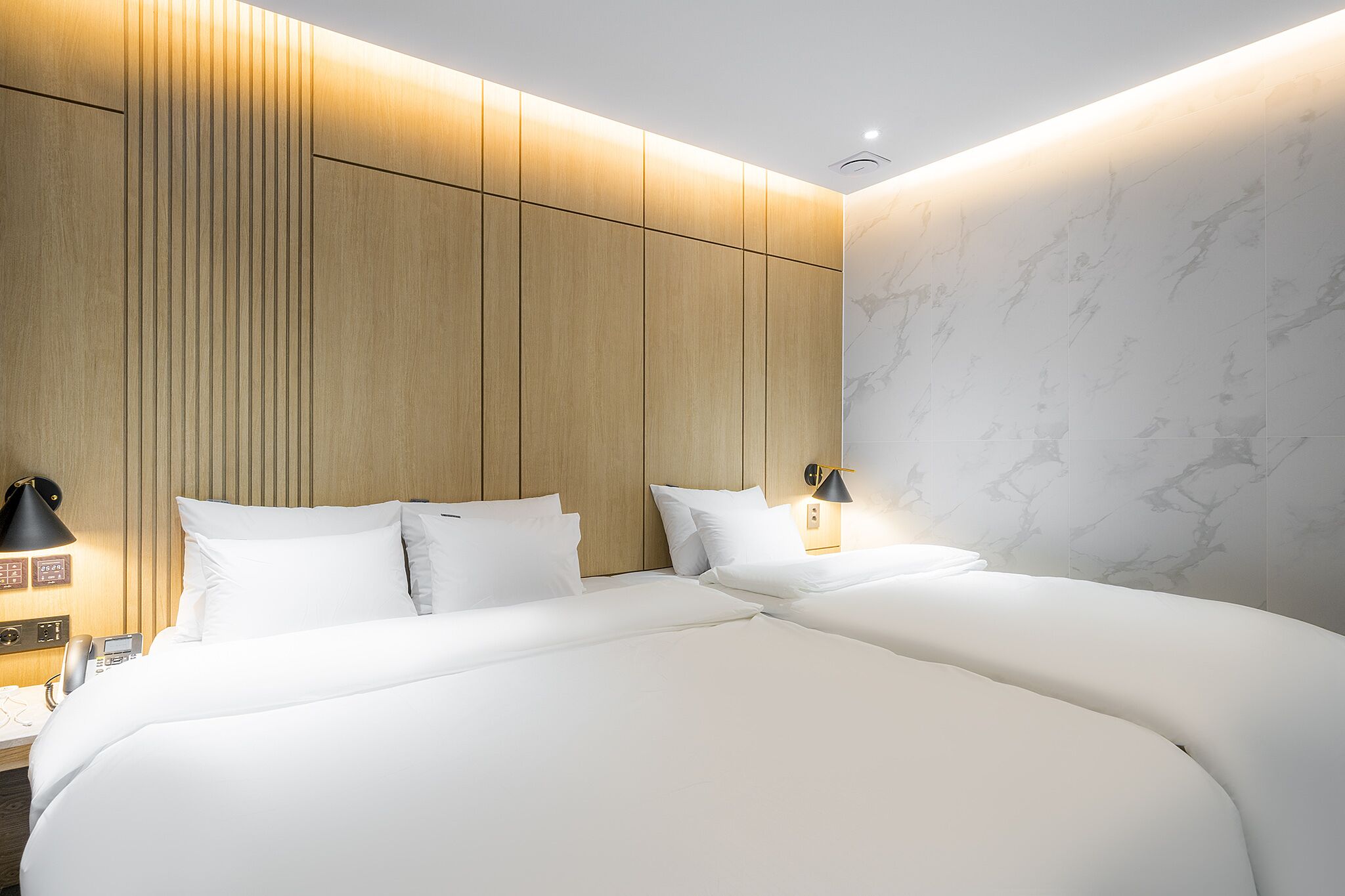 A modern hotel room with a large bed, wooden paneling on the walls, and a marble-patterned wall.