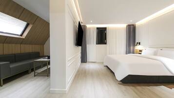 Ein modernes Hotelzimmer mit einer Couch, einem Bett, einem Fernseher und einem Schreibtisch.