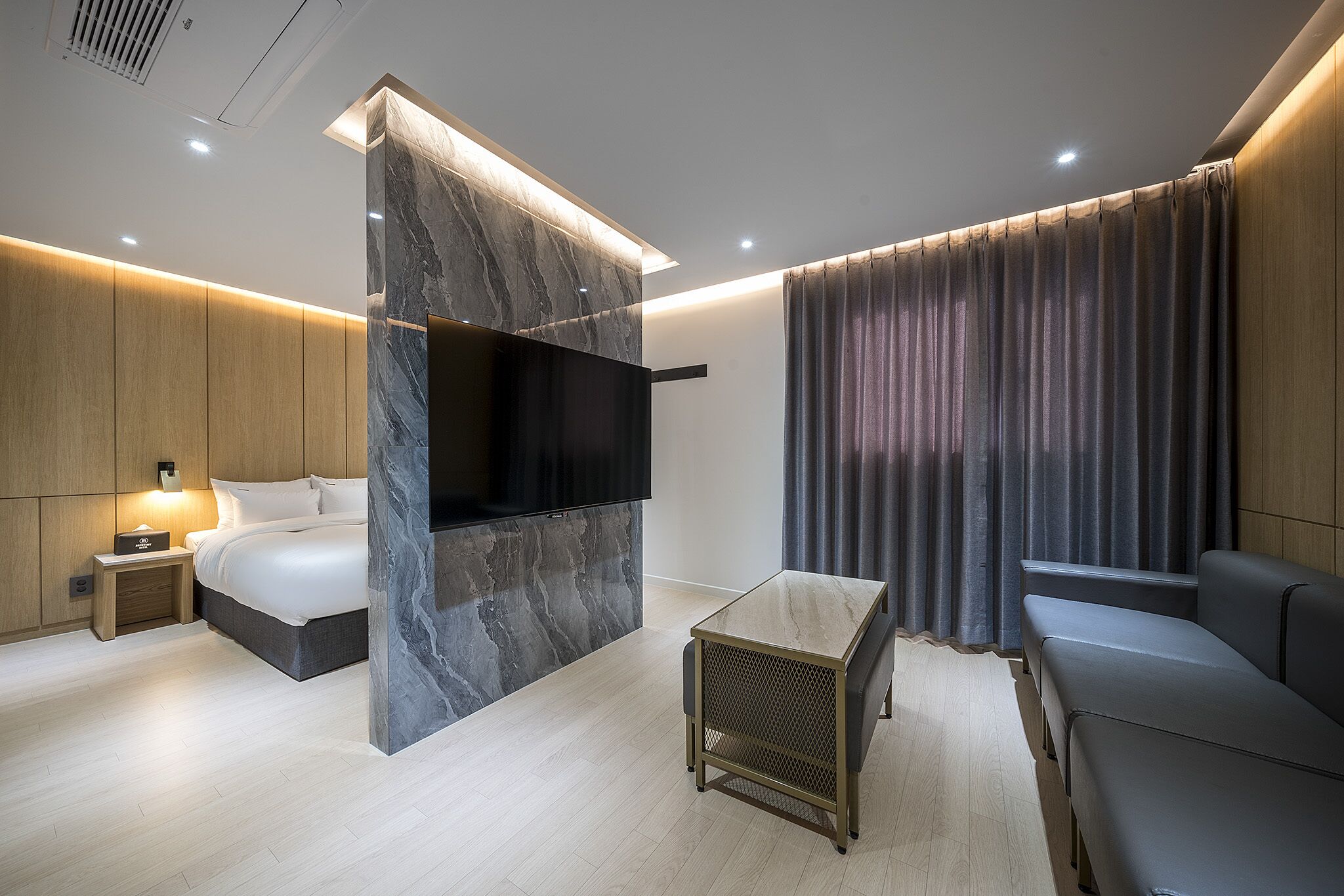 Ein modernes Hotelzimmer mit Bett, Fernseher, Sofa und einem kleinen Tisch.