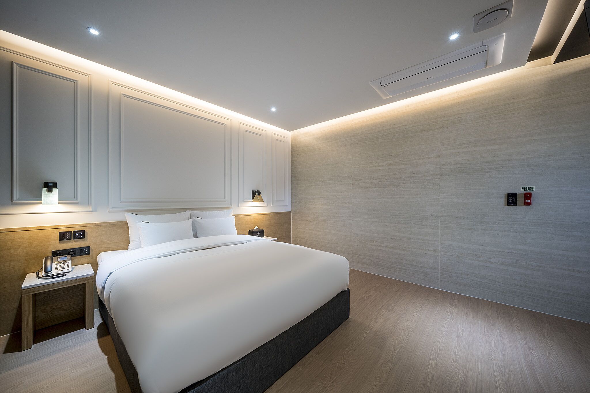 Quarto de hotel moderno com cama grande, mesas de cabeceira, espelho e ar condicionado fixado na parede.