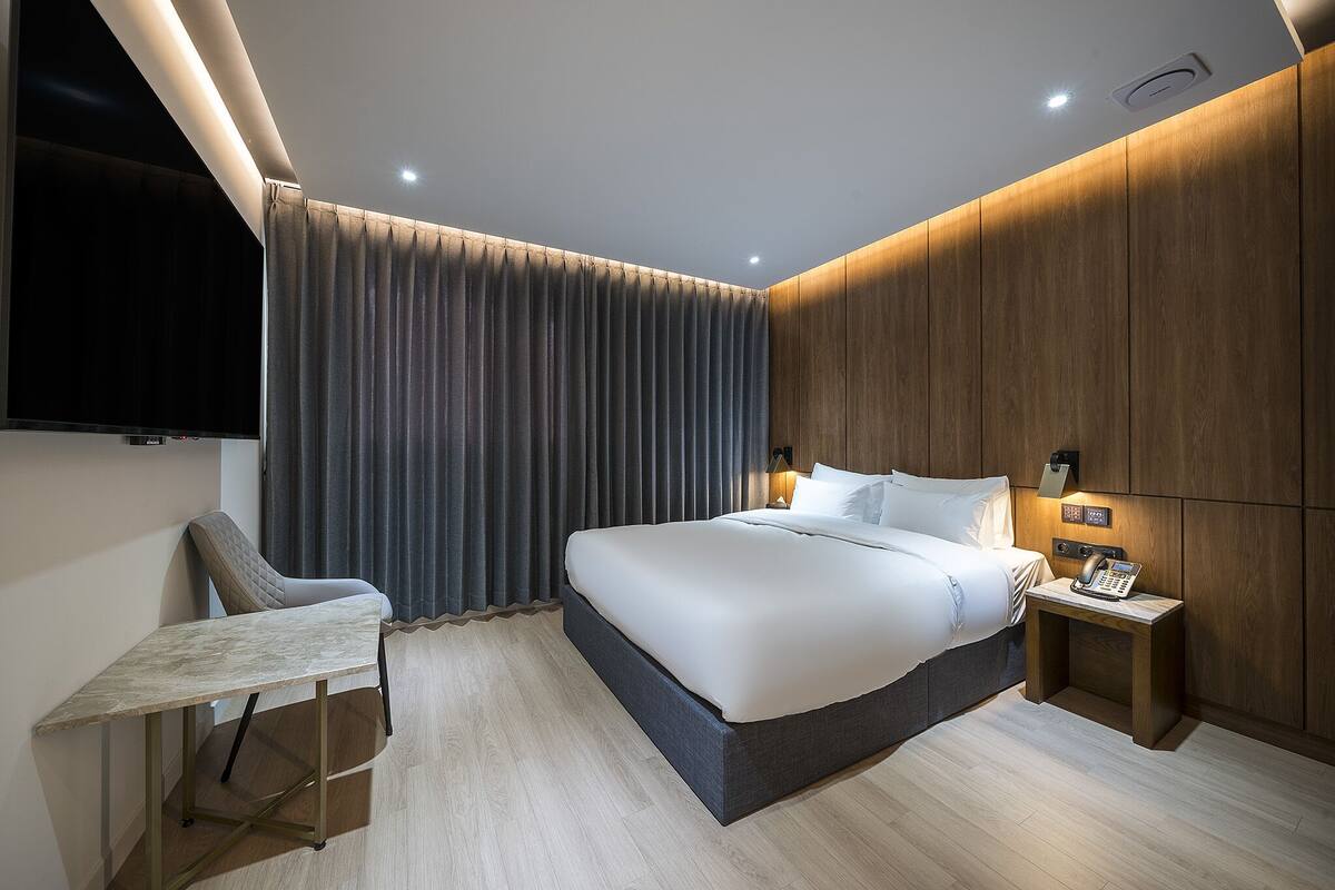 Ein modernes Hotelzimmer mit einem großen Bett, einem Schreibtisch und einem an der Wand befestigten Fernseher.