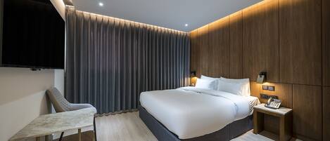 Una habitación de hotel moderna con una cama grande, un escritorio y un televisor montado en la pared.