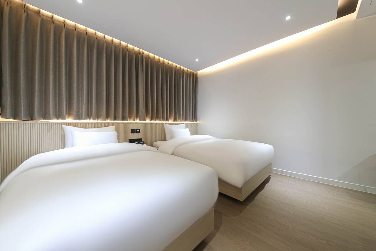 Ein modernes Hotelzimmer mit zwei Betten, einem großen Fenster mit Vorhängen und Holzboden.