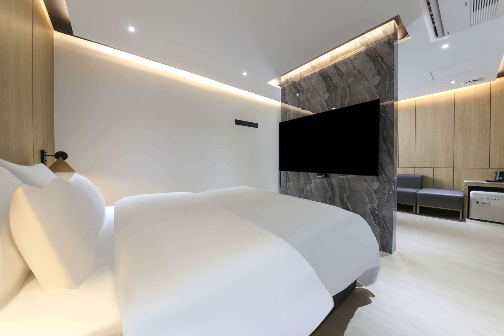 Um quarto moderno com uma cama grande, uma televisão de tela plana fixada numa parede de mármore e um espaço de estar com uma mesinha e cadeiras.