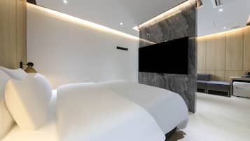 Um quarto moderno com uma cama grande, uma televisão de tela plana fixada numa parede de mármore e um espaço de estar com uma mesinha e cadeiras.