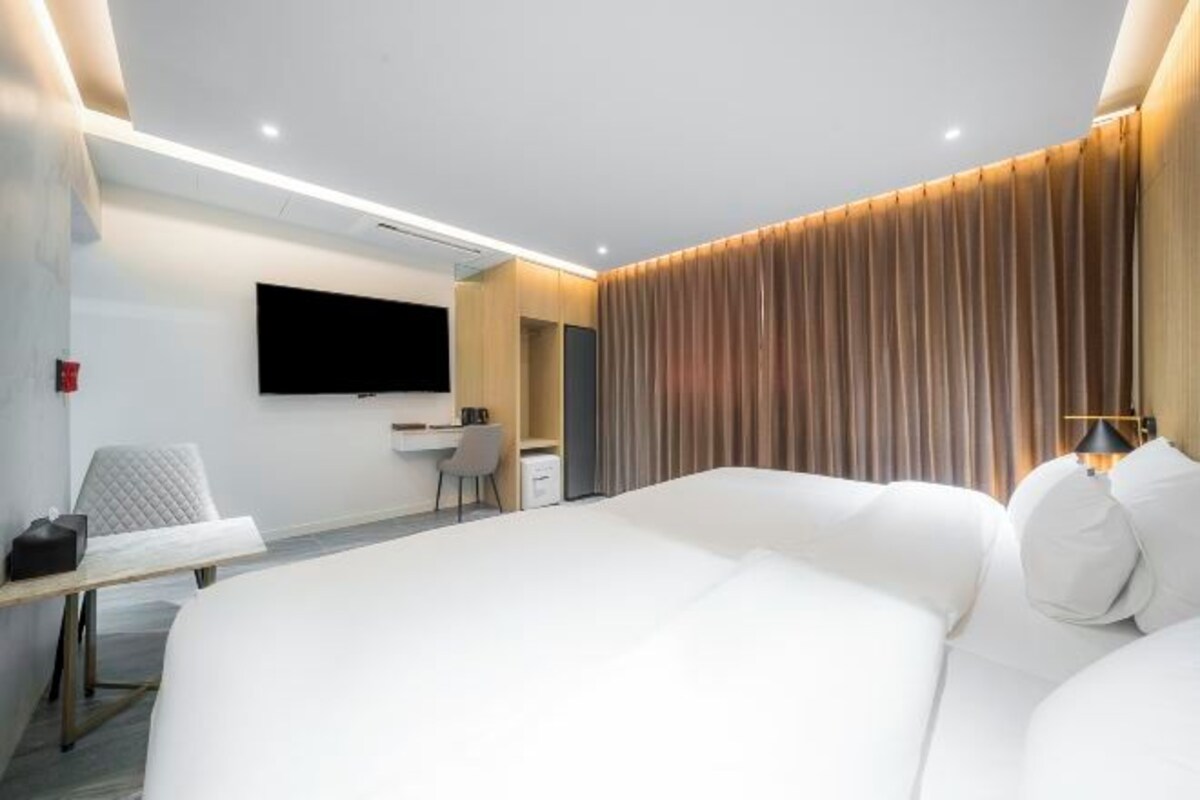 A modern hotel room with a large bed, a desk, a flat-screen TV, and a curtain-covered wall.