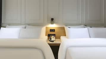 A hotel room with two beds, a bedside table with a phone, and a wall-mounted light.