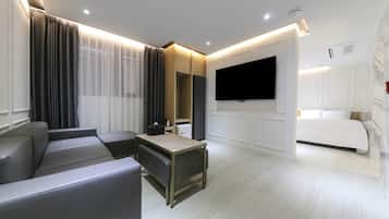 A modern hotel room with a sofa, a TV mounted on the wall, a bed, and a small kitchenette area.