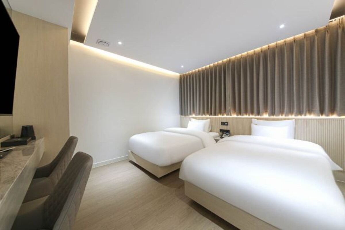 A modern hotel room with two beds, a desk, and a large window with curtains.