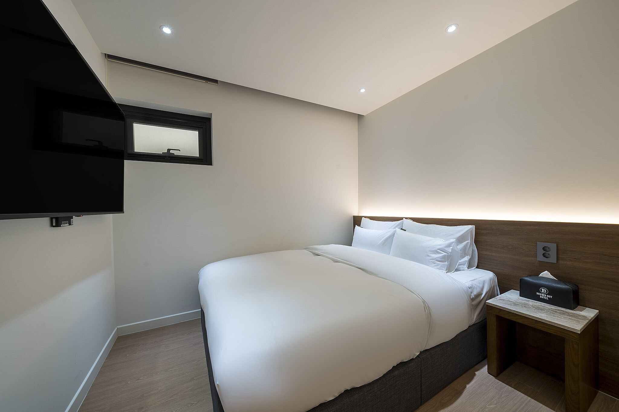 Een moderne slaapkamer met een groot bed, een nachtkastje met lamp en een aan de muur bevestigde televisie.