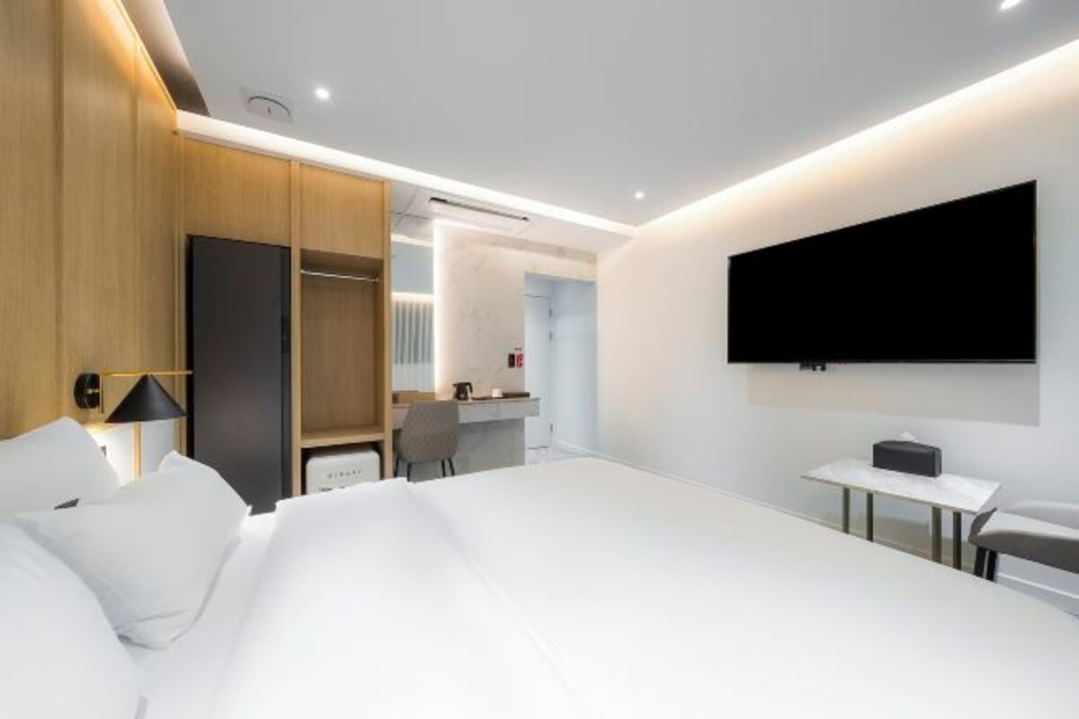 A modern hotel room with a large bed, a desk, a chair, and a TV mounted on the wall.