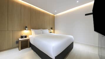 A modern hotel room with a large bed, wooden paneling on the walls, a bedside table with a lamp, and a flat-screen TV mounted on the wall.