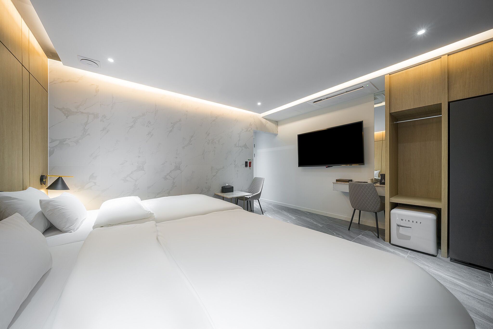 Una habitación de hotel moderna con una cama grande, un escritorio, una silla, un televisor y un armario.