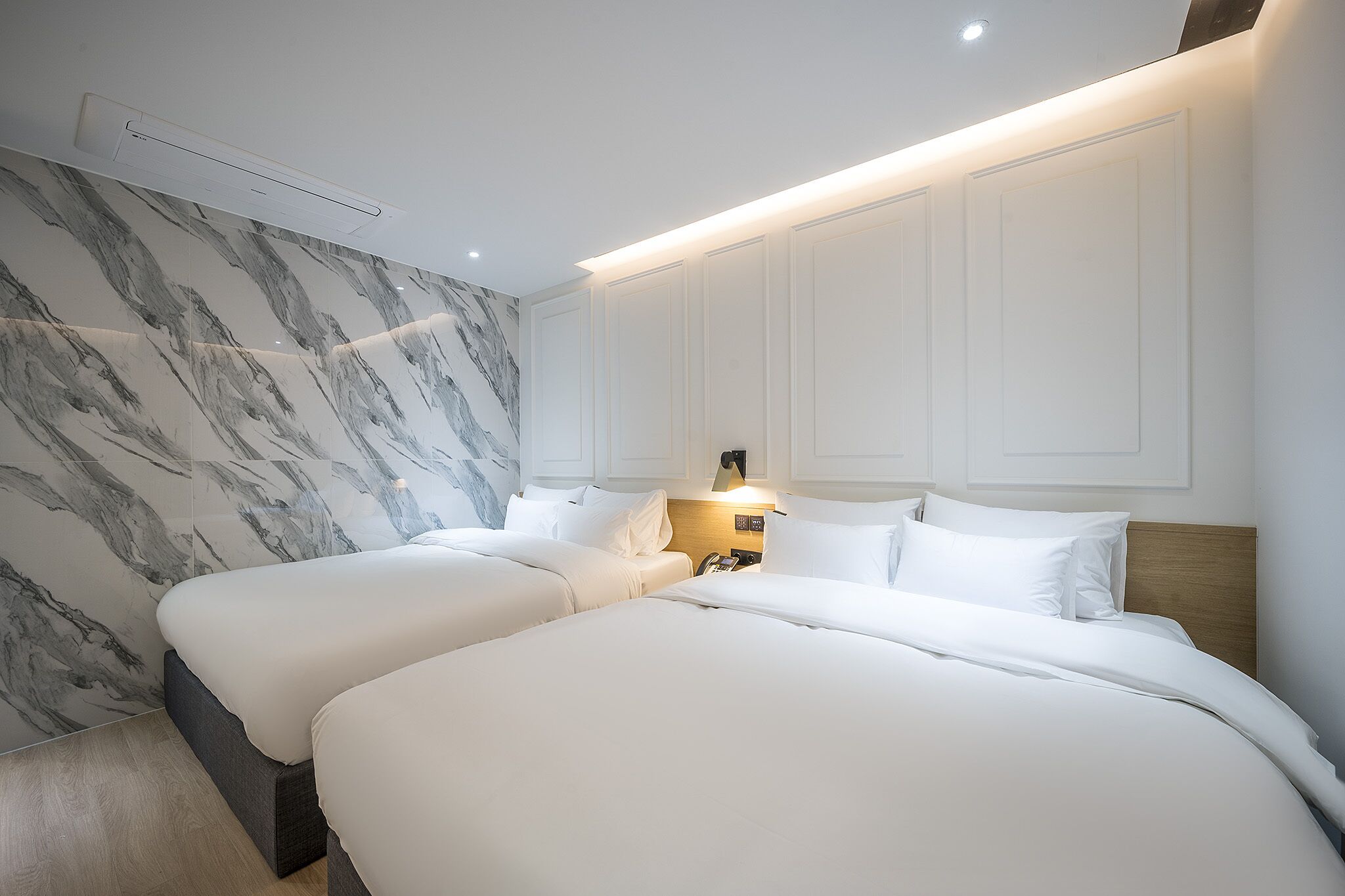Et hotelværelse med to senge, vægge med marmorlignende mønster og et moderne design.